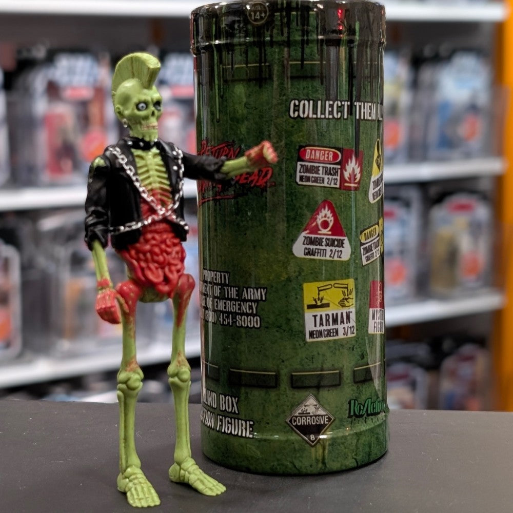 Super7 neon green male zombie figure with mohawk, skeletal torso, exposed red intestines, and black jacket with chains standing beside collectible tube