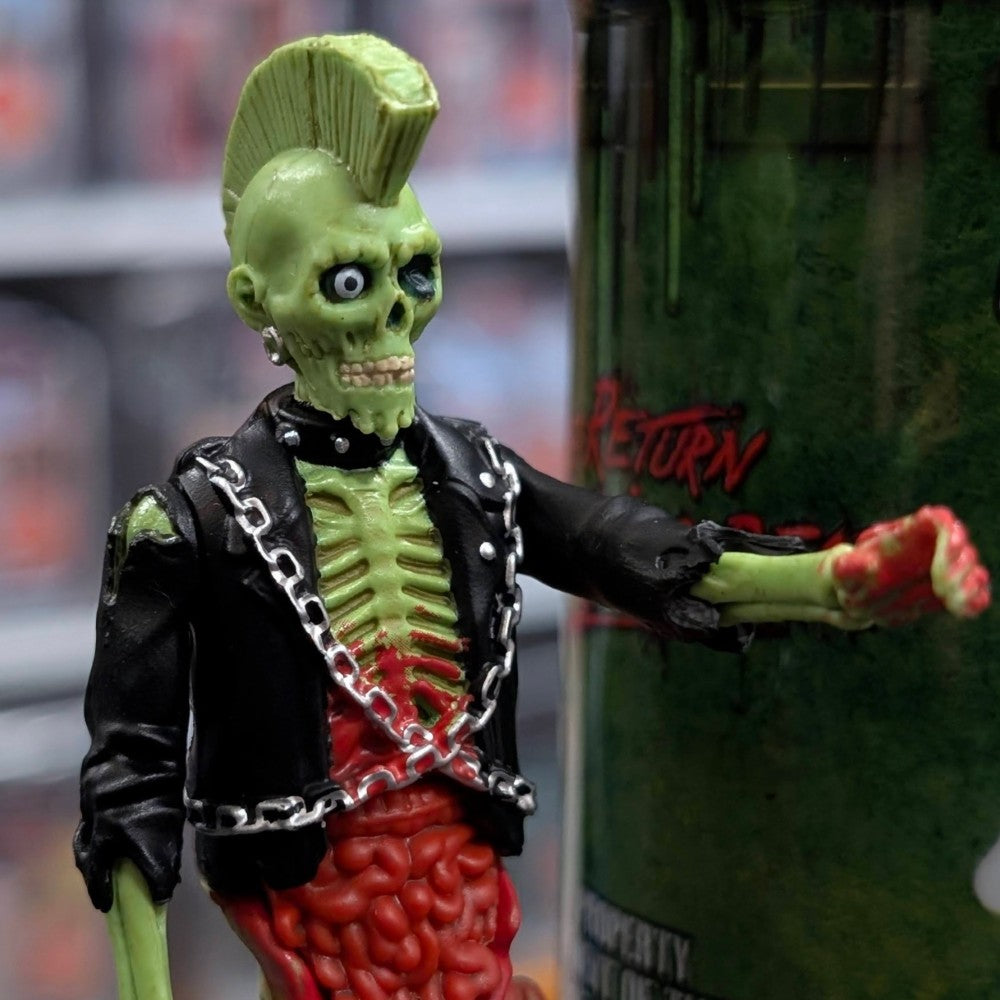Super7 neon green male zombie figure with mohawk wearing black jacket and chains reaching forward near green collectible tube
