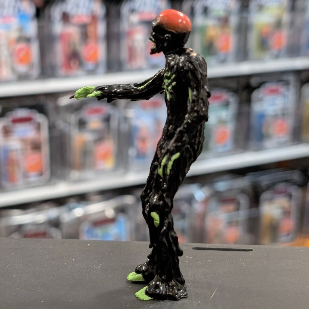 Super7 Tarman zombie figure covered in glossy neon green tar with red brain detail posed sideways on display surface