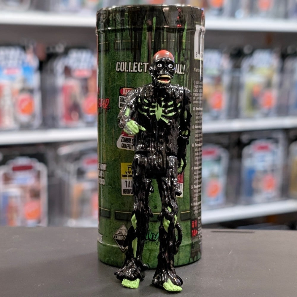 Super7 black tar-covered Tarman zombie figure with glowing green skeletal details standing in front of collectible container