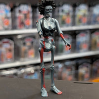 Super7 “Trash” metallic gray female zombie figure with red accents and spiked hair posed on store counter