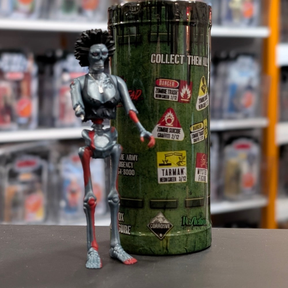Super7 metallic blue graffiti female zombie figure with spiked hair and torn red accents standing in front of collectible tube