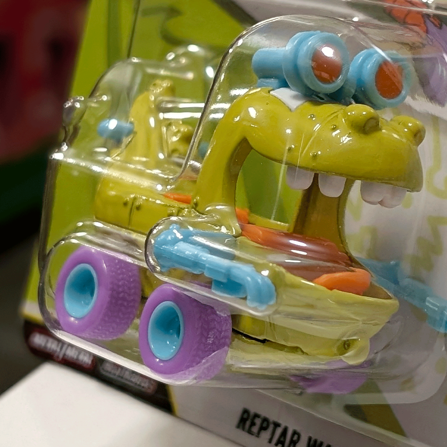 Mattel Hot Wheels Rugrats Reptar Car die-cast vehicle with purple wheels and blue goggles in clear packaging side view