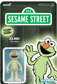 Pale green glowing Elmo figure with orange nose and wide eyes in clear blister pack against Sesame Street backdrop