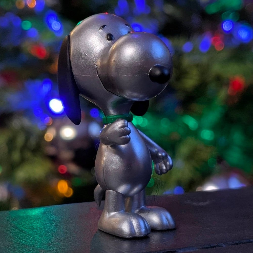 Silver Snoopy figure in metallic finish from Super7 with holiday lights and decorated tree background