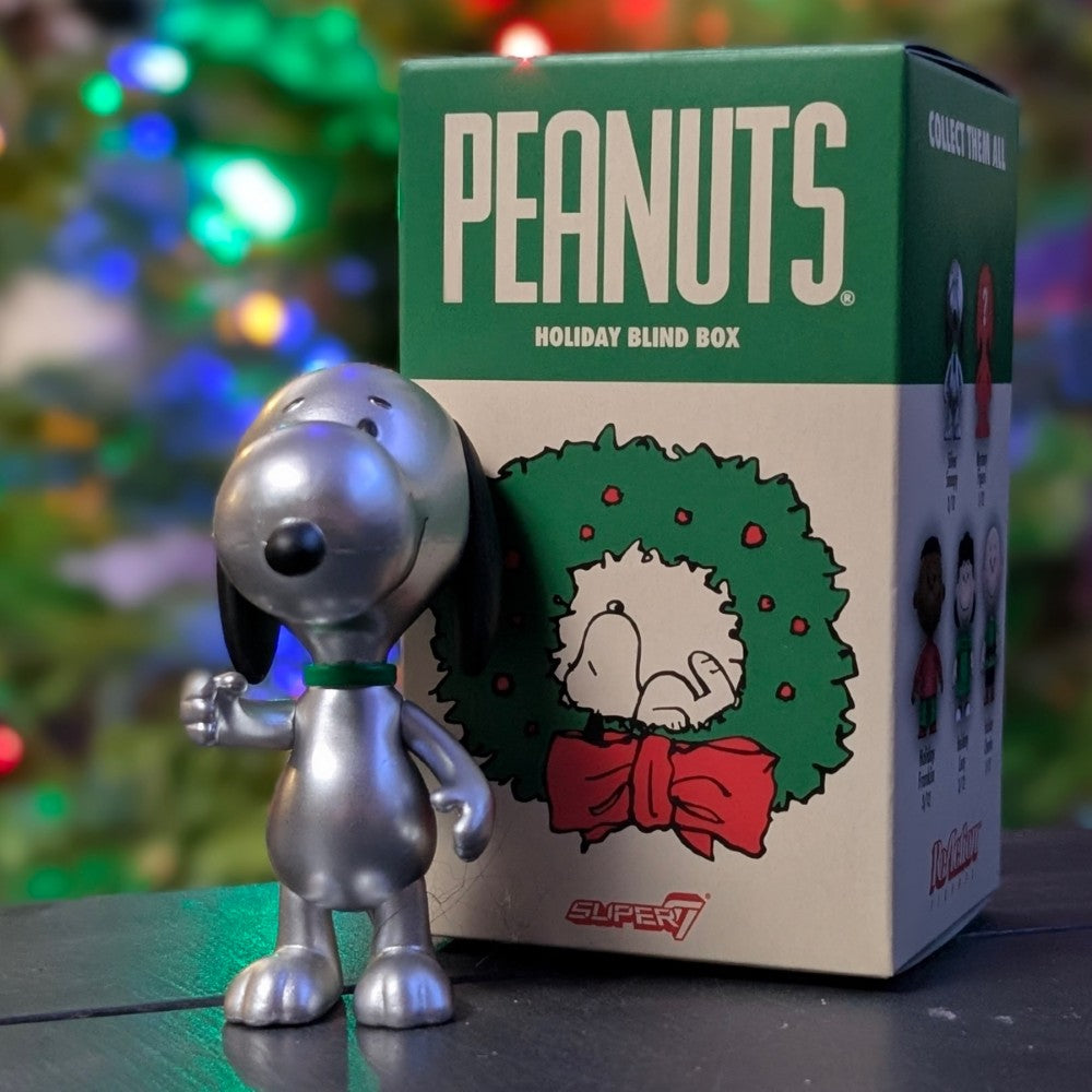 Silver Snoopy metallic holiday ReAction figure standing next to Super7 Peanuts Holiday Blind Box packaging