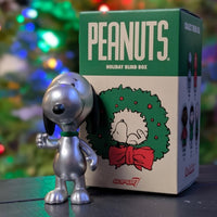 Silver Snoopy metallic holiday ReAction figure standing next to Super7 Peanuts Holiday Blind Box packaging