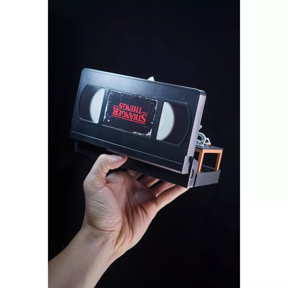 Hand holding VHS Stars Stranger Things Eleven vs. Demogorgon Diorama Playset by Console Heroes against black background.