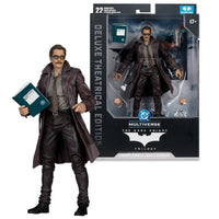 Multiverse The Dark Knight: Batman - The Dark Knight: Theatrical Edition action figure shown next to its retail packaging. The figure is dressed in a dark brown trench coat, gray shirt, and black pants, holding a teal book.