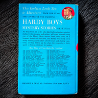 Back cover of 1959 Hardy Boys book The Tower Treasure with blue background and list of titles by Grosset & Dunlap