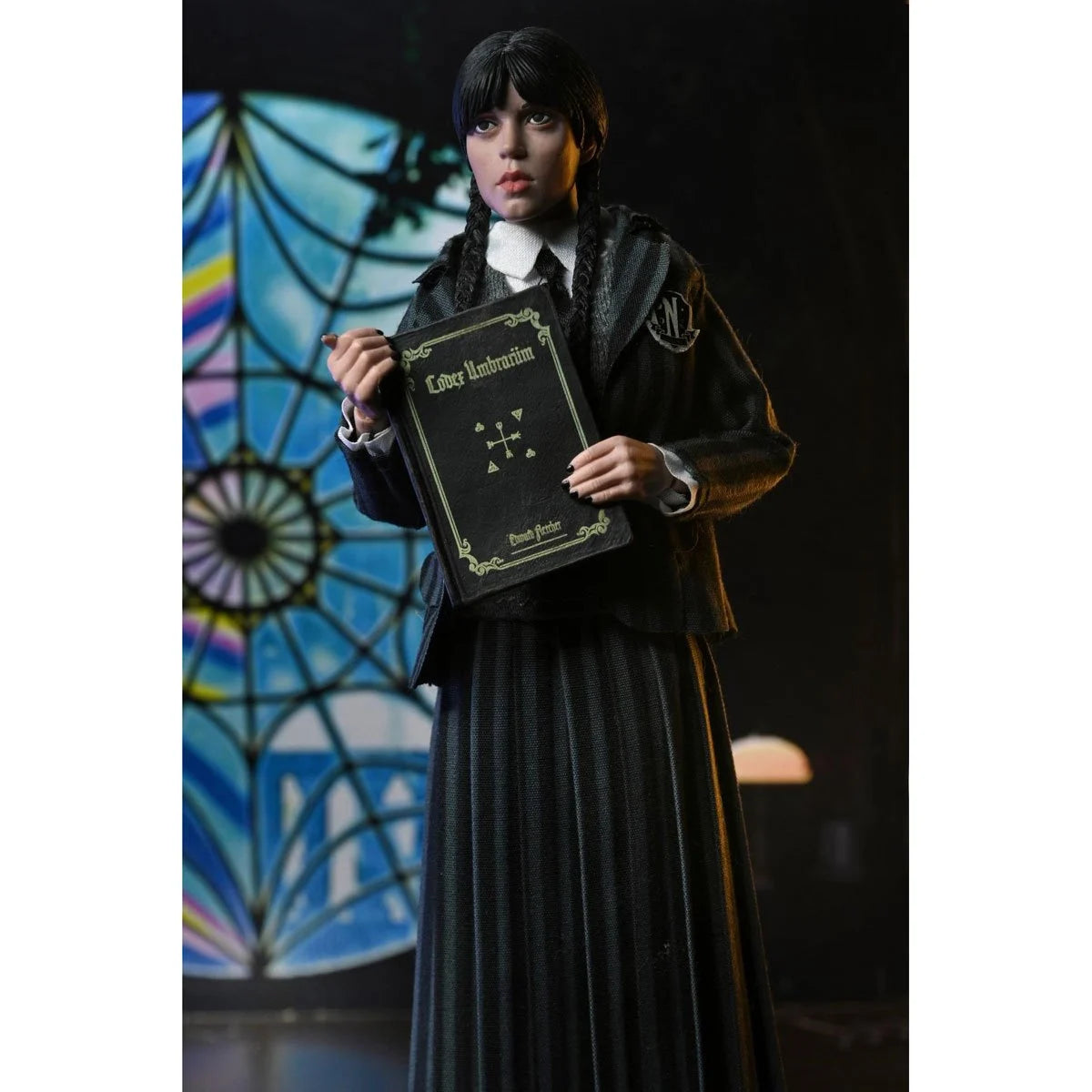Clothed action figure of a dark-haired girl in gothic school uniform holding a book against stained glass background