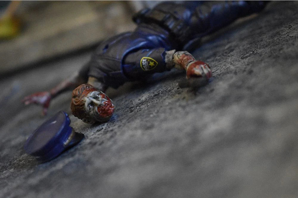 Toy figure of a character in a blue outfit lying on a textured surface with a bottle cap nearby.