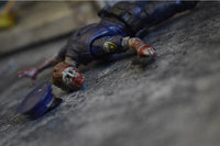 Toy figure of a character in a blue outfit lying on a textured surface with a bottle cap nearby.