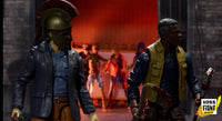 Two action figures in a dramatic setting with a brick wall and red smoke in the background.