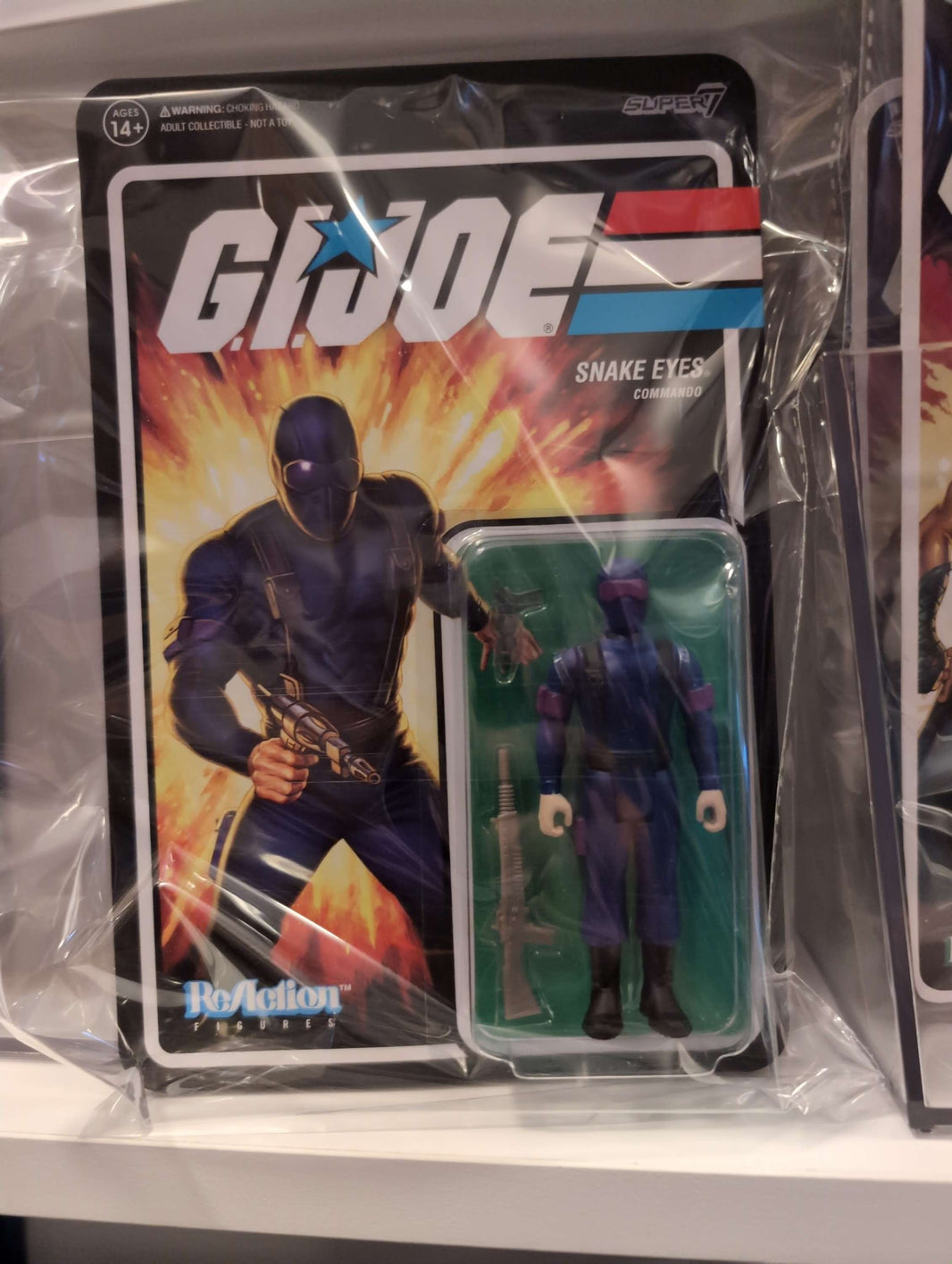 GI Joe Snake Eyes action figure in original Super7 packaging with illustrated fiery background and weapon accessory
