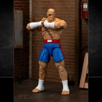 Jada Toys Ultra Street Fighter II Sagat action figure in blue shorts and wrap hands posed in industrial setting