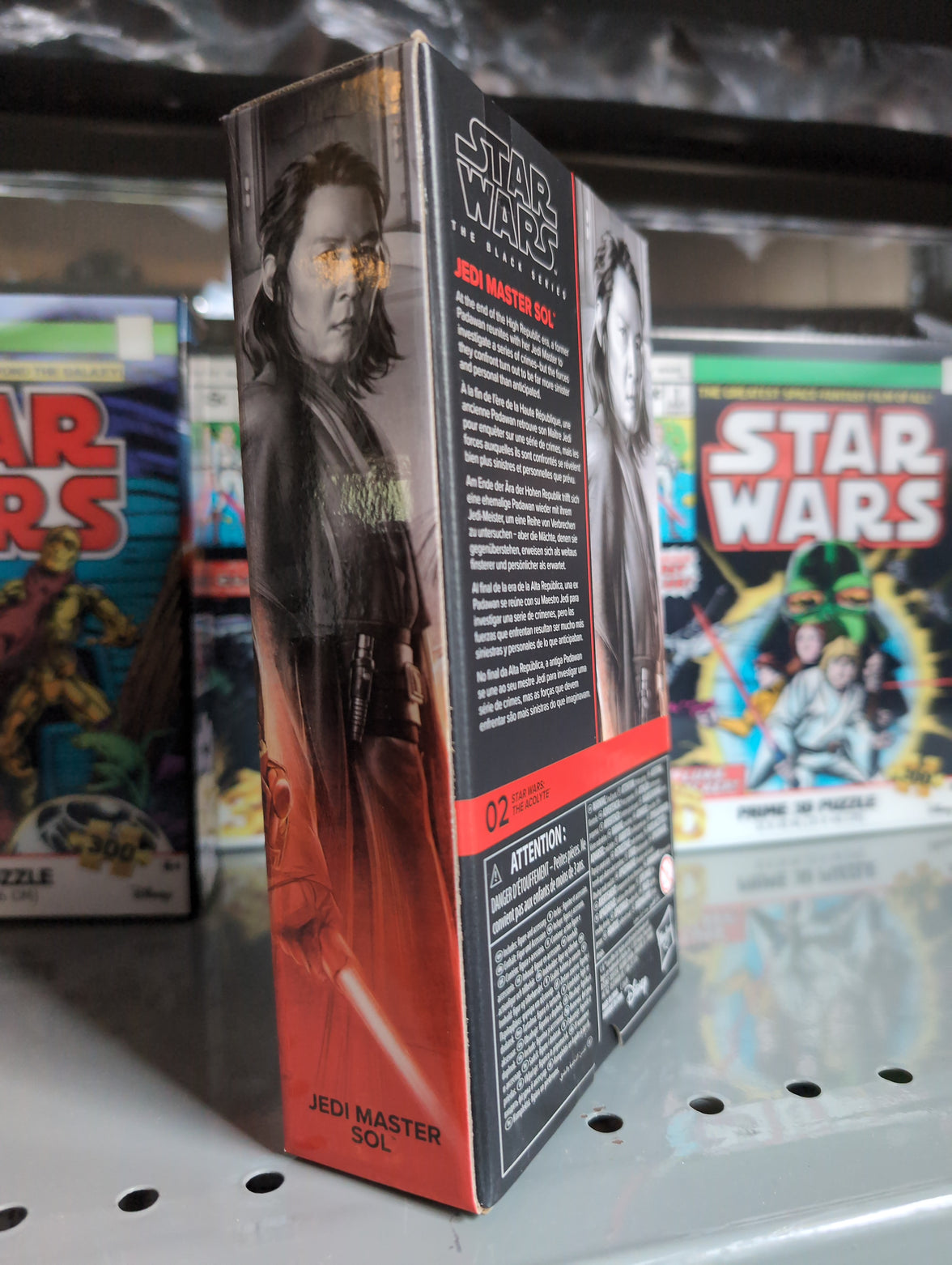Hasbro Star Wars Black Series Jedi Master Sol action figure box showing character art and details on shelf with puzzles behind