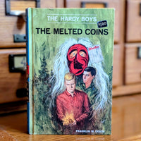 Vintage 1970 Hardy Boys book The Melted Coins by Grosset & Dunlap featuring two boys and a red mask on cover